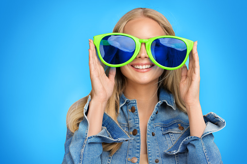 Happy Teenage Girl in Party Eyeglasses having Fun. Smiling Young Woman in Big Glasses watching Blue Screen. Portrait of Cheerful Teenager Female playing Game