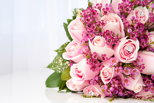 Pink roses with faux diamond accent and filler flower wedding bouquet on table.