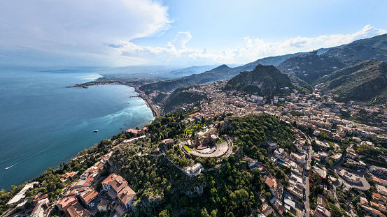 Taormina Cityscape on top of coastal hills. Drone Point of view over the famous ancient Greek Theatre of Taormina - Teatro Greco from the third century BC. Taormina Coast towards the ionian sea in the background. XXXL Aerial Panorama. Taormina, Messina Province, Sicily, Southern Europe, Europe