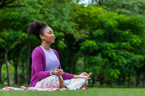 African American woman relaxingly practicing meditation in the forest to attain happiness from inner peace wisdom for healthy mind and soul