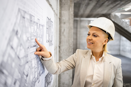 Female construction engineer or contractor looking at blueprint plan of the building.