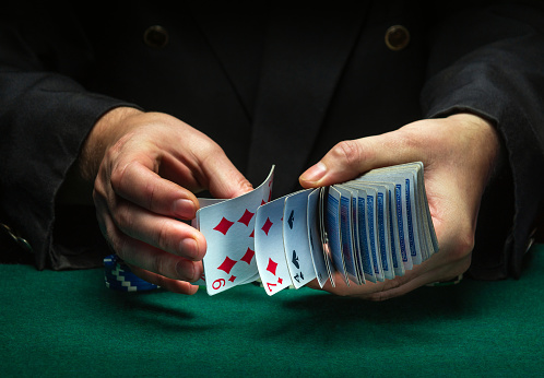 A professional dealer or croupier quickly shuffles playing cards in a club at a green table with playing chips. The concept of a successful poker game in a casino