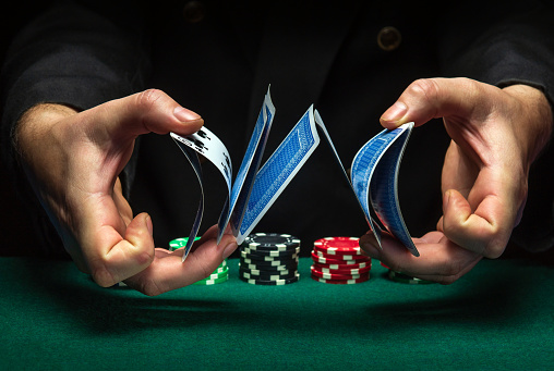 Masterly shuffling of playing cards with the hands of a dealer or croupier in a poker club on a green table with playing chips. Casino game concept.