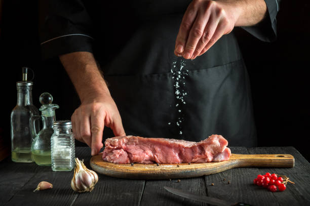 le cuisinier prépare de la viande de veau crue. avant la cuisson, le chef ajoute du sel au bœuf. un plat national est préparé dans la cuisine du restaurant. - veal calf meat baking photos et images de collection