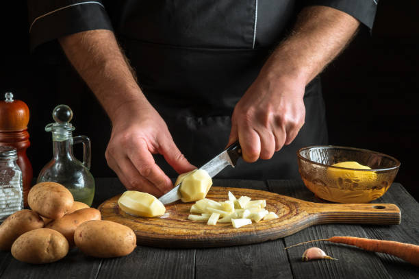 istock Professional chef cuts raw potatoes into pieces with a knife before preparing breakfast or dinner. Close-up of a cook hands while working in a restaurant kitchen 1494504836