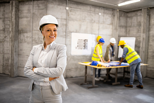 Portrait of successful female architect in business suit and hard hat standing at construction site.