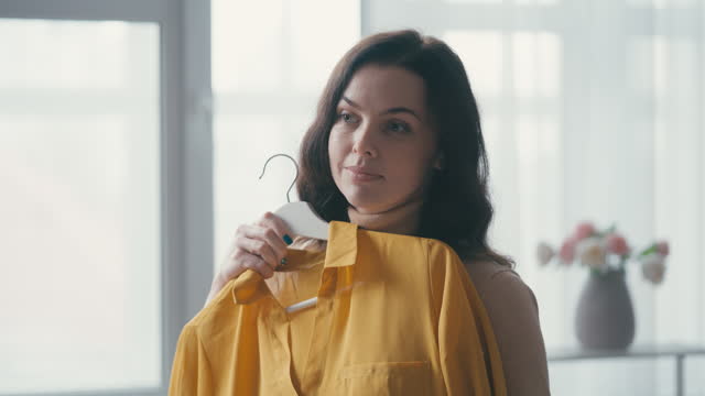 Beautiful middle-aged woman trying on clothing at home, preparing for event