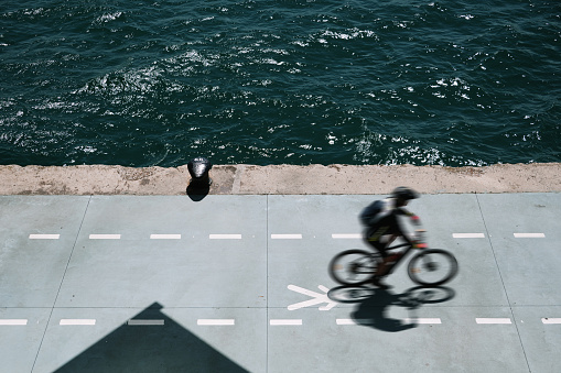 An anonymous cyclist riding his bicycle on a bicycle lane by the sea. Aerial view.