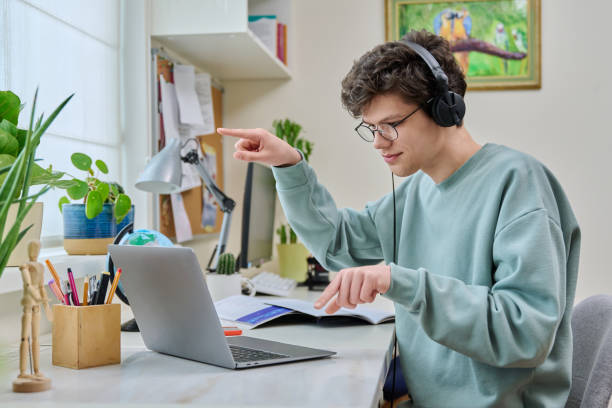 Teenage male student having video conference, talking looking at webcam on laptop stock photo
