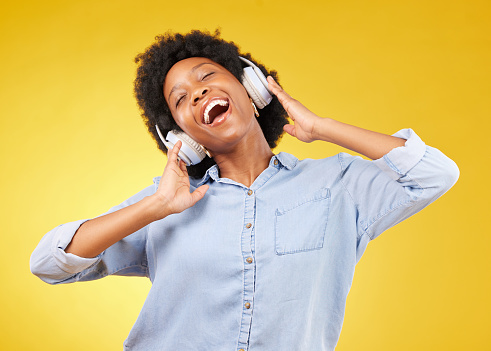 Black woman, headphones and freedom, listening to music and happiness with dance on yellow studio background. Happy female, carefree and sing along to radio, audio streaming with fun and technology