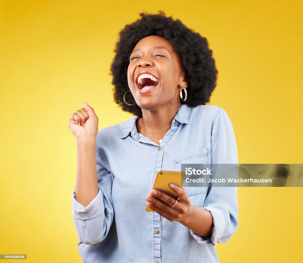 Happy, excited and phone with black woman in studio for text message, notification and social media news. Deal, winner and celebration with girl on yellow background for offer, giveaway and surprise Happiness Stock Photo
