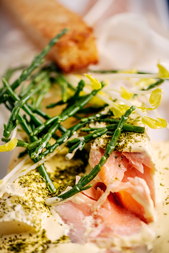 Close-up of a slice of salmon that has been poached and served with hollandaise sauce, asparagus shoots and asparagus shavings and salicornia. Colour, vertical format with some copy space.