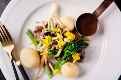 Overhead view of a dish of veal steak served with broccoli, enoki mushrooms, new potatoes, decorated with canola flowers with a port flavoured sauce. Colour, horizontal format with some copy space. Photographed on location at a restaurant on the island of Moen in Denmark.