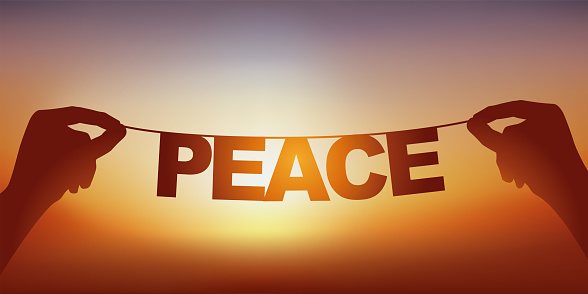 The silhouette of the word peace written in loose letters on a garland against a sunset.