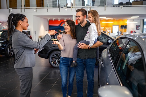 Sales person giving car key to family in car dealership