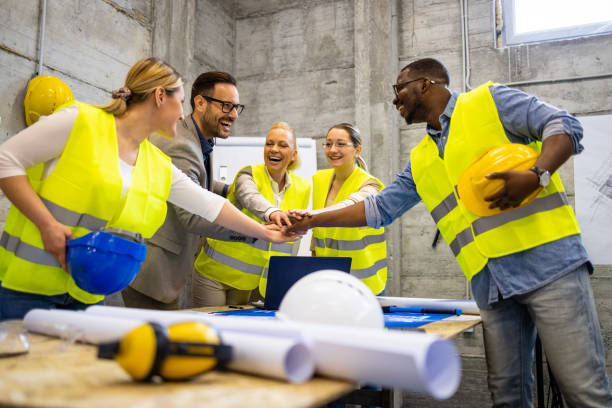 istock Team of structural engineers and architects holding hands together above building plans and blueprints at construction site. 1494515536