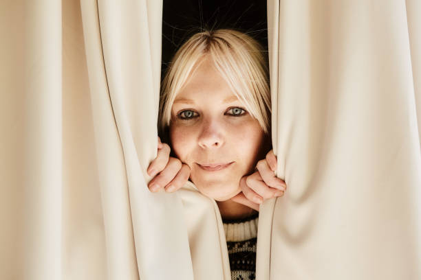 istock Young woman looking through curtains with an enigmatic smile 1494523608