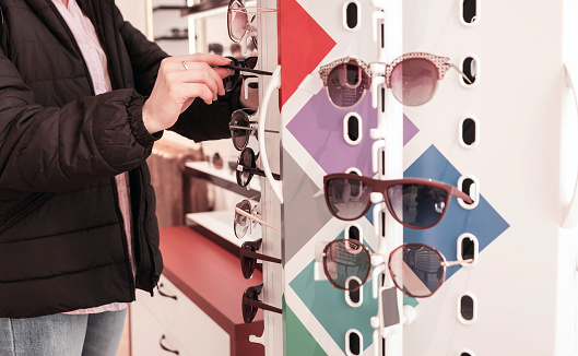 woman chooses sunglasses on a shelf in a store. A stand with glasses in an optics store