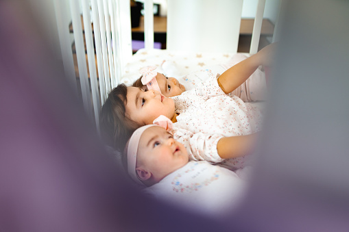 Cute little girls lying in a crib together and looking up