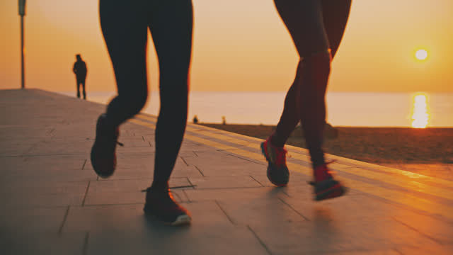 SLO MO of female friends jogging at promenade. Idyllic view of sea at sunrise. They are exercising at dawn