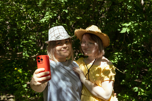 Russia, Kopeysk, June, 2022. Two Asian smiling mother and daughter in summer hats take selfies-self-portrait photos on an iPhone. A carefree, joyful mother and daughter take selfies on a summer day