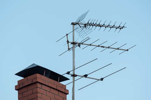 TV antenna on red roof. television antenna on roof with blue sky. Brick pipe house and media transmitter, radio, television