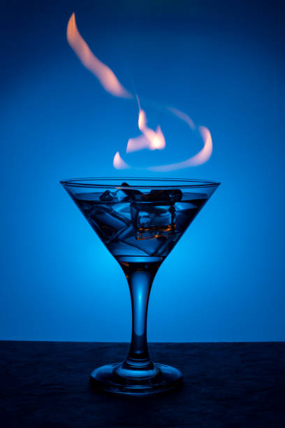 brennendes alkoholisches getränk mit eiswürfeln auf blauem farbverlaufshintergrund. brennbarer cocktail auf dem tisch in einer bar - martini brand vermouth stock-fotos und bilder