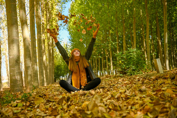 Woman covering her face with green leaf, looking at the camera with smile on her face.