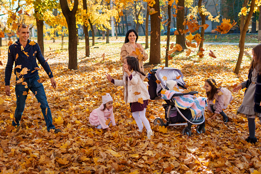 portrait of a big family in autumn city park, happy children and parents playing together and throwing yellow leaves, beautiful nature, bright sunny day