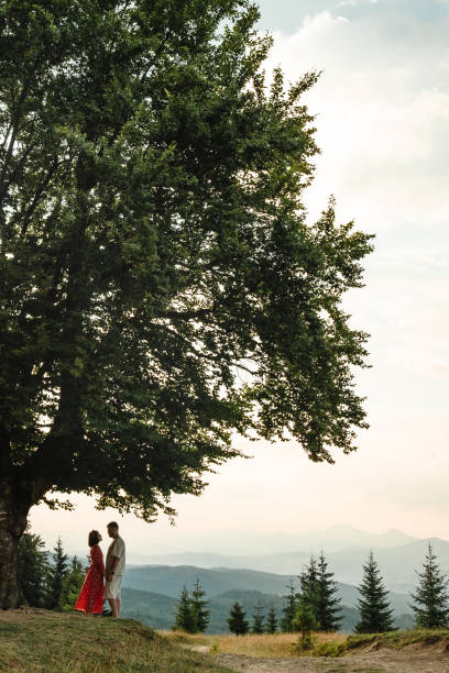 a couple stands and looks at each other on a bench by a big old beech tree with a view of the carpathians mountains