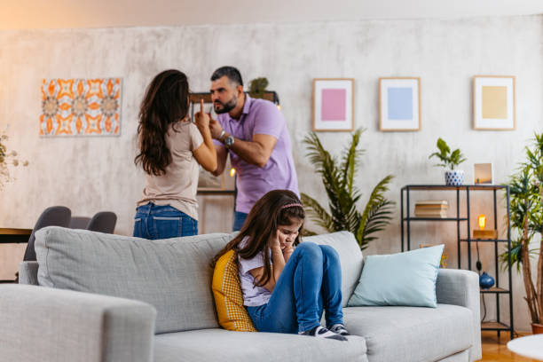 Little Girl Covering Her Ears While Her Parents Are Arguing Behind Her Little girl blocking her ears while her parents are arguing behind her in the living room. arguing couple divorce family stock pictures, royalty-free photos & images