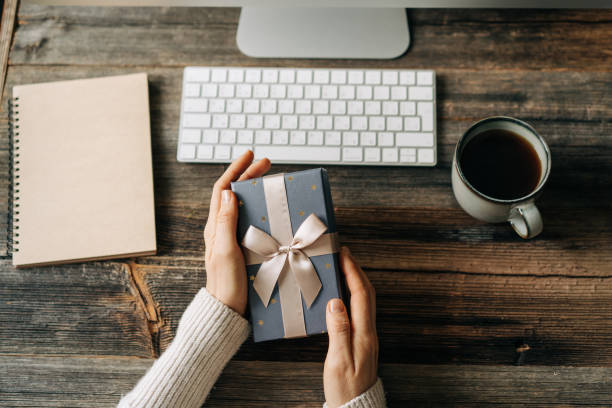 istock Top view of a gift box in female hands over a working office table. 1494543187
