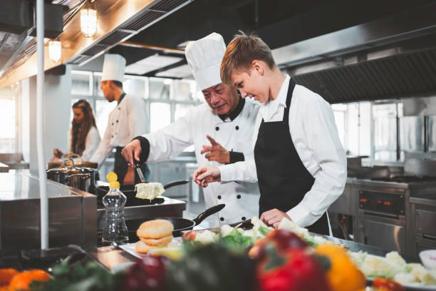 chef enseignant aux élèves à cuisiner dans la cuisine d’une école de cuisine - établissement de restauration photos et images de collection