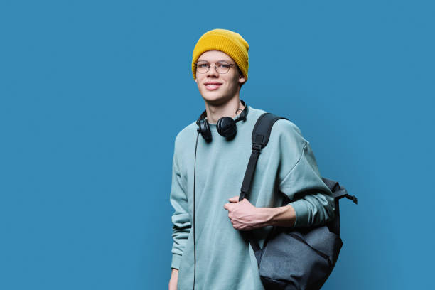 istock Young male in yellow cap sweatshirt with headphones backpack on blue background 1494550331