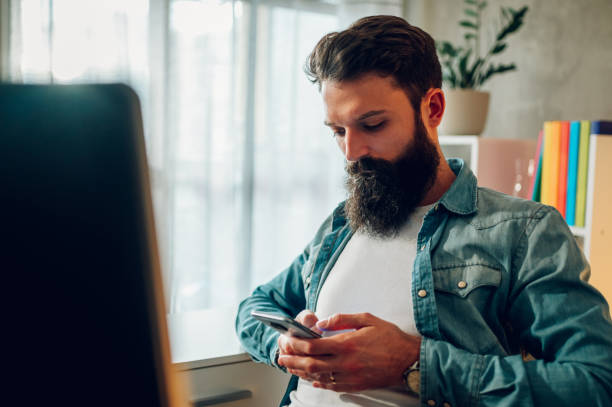 istock A focused bearded freelancer is sitting at his home office and communicating with his client on the phone while typing e-mails and messages. 1494559894