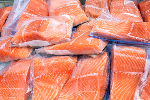 Closeup view of a pile of pieces of raw salmon packaged in small plastic bags on farmers market stand
