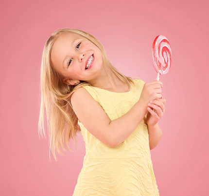 Candy, happy and lollipop with portrait of girl in studio for sugar, party and carnival food isolated on pink background. Cute, positive and youth with child and eating snack for playful and treats