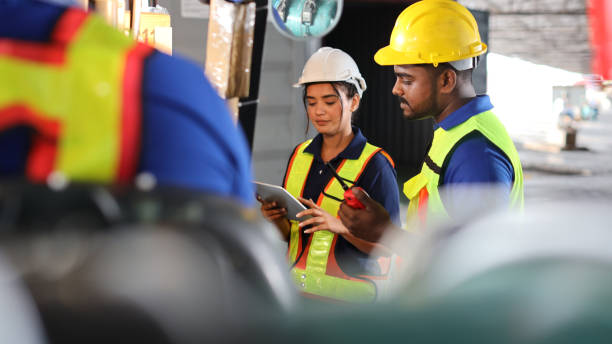 istock Group of warehouse workers with hardhats and reflective jackets using tablet, walkie talkie radio and cardboard while controlling stock and inventory in retail warehouse logistics, distribution center 1494568554