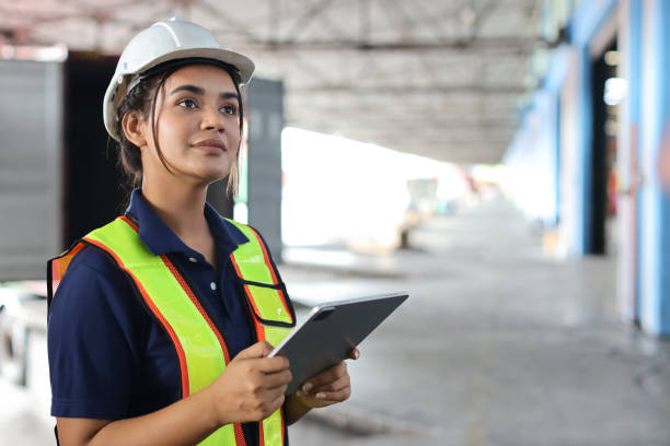 istock Warehouse workers woman with hardhats and reflective jackets using tablet, walkie talkie radio while looking away and controlling stock and inventory in retail warehouse logistics, distribution center 1494568584