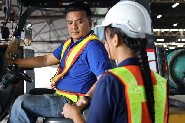 istock Warehouse worker or forklift driver man with hardhats and reflective jackets in vehicle sending forklift key to colleague woman trainee at inventory in retail warehouse logistics, distribution center 1494568679