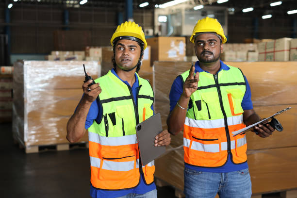 istock Group of warehouse workers with hardhats and reflective jackets using tablet, walkie talkie radio and cardboard while controlling stock and inventory in retail warehouse logistics, distribution center 1494568702