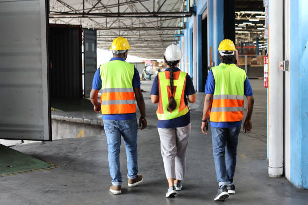 istock Group of warehouse workers with hardhats and reflective jackets using tablet, walkie talkie radio and cardboard while controlling stock and inventory in retail warehouse logistics, distribution center 1494568767