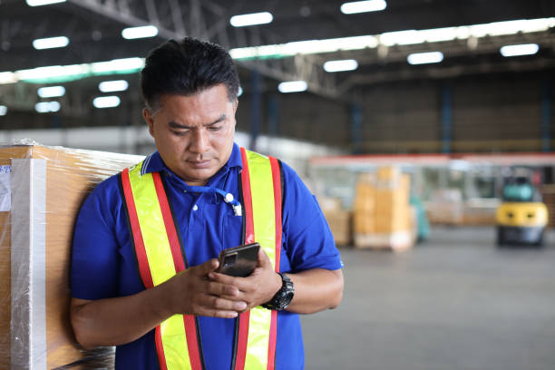 istock Warehouse workers man with hardhats and reflective jackets using smart mobile phone, walkie talkie radio controlling stock and inventory in retail warehouse logistics, distribution center 1494568770