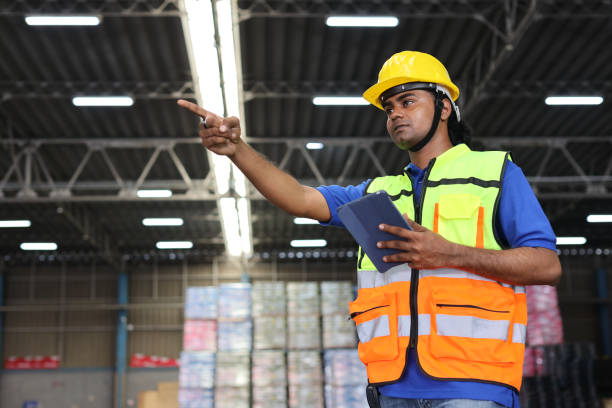 istock Warehouse workers man with hardhats and reflective jackets using tablet, walkie talkie radio and cardboard while controlling stock and inventory in retail warehouse logistics, distribution center 1494568825