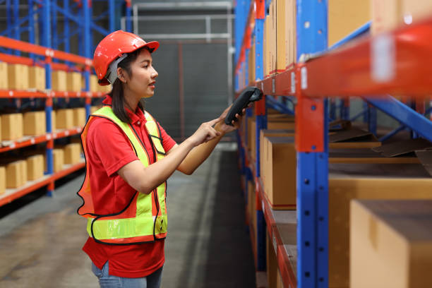 istock Warehouse workers woman with hardhats and reflective jackets scanning barcode on large box package for delivery to production stock and inventory in retail warehouse logistics, distribution center 1494569419