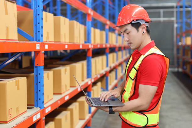 istock Warehouse workers man with hardhats and reflective jackets using computer, walkie talkie radio and cardboard while controlling stock and inventory in retail warehouse logistics, distribution center 1494569532