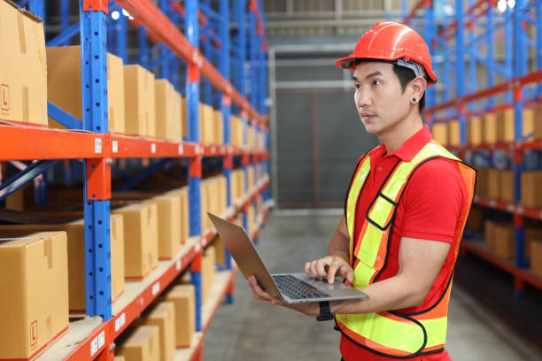 istock Warehouse workers man with hardhats and reflective jackets using computer, walkie talkie radio and cardboard while controlling stock and inventory in retail warehouse logistics, distribution center 1494569542