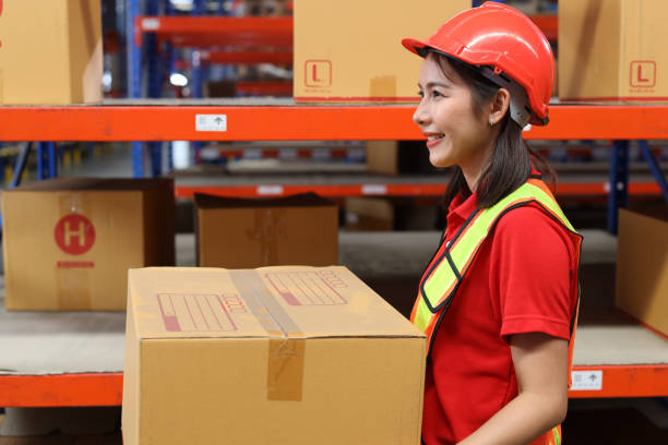istock Side view asian warehouse workers woman with hardhats and reflective jackets carrying a large box for delivery to production stock and inventory in retail warehouse logistics, distribution center 1494570676