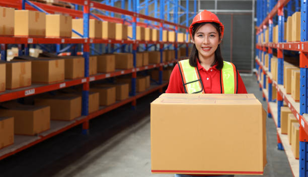 istock Asian warehouse workers woman with hardhats and reflective jackets carrying a large box for delivery to production stock and inventory in retail warehouse logistics, distribution center 1494570689