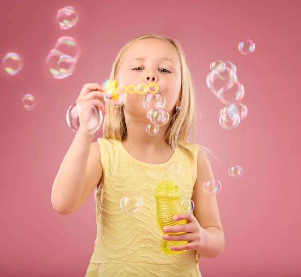 istock Portrait, fun and girl blowing bubbles, content and playing in studio while posing against pink background. Hand, face and child enjoying freedom, toy and innocent magic while standing isolated 1494571341